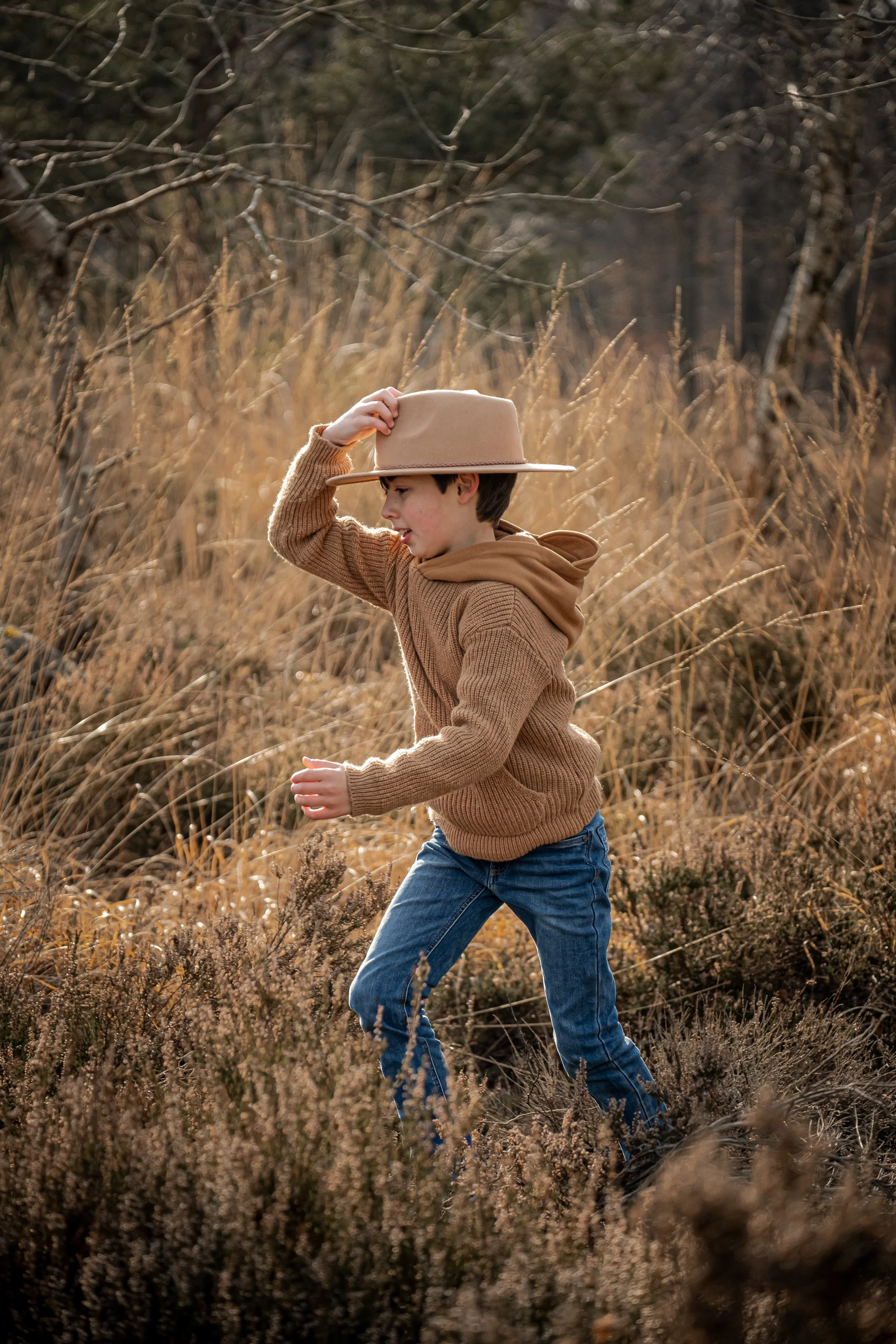 portrait du grand frere qui court dans la nature et retient son chapeau sur sa tete