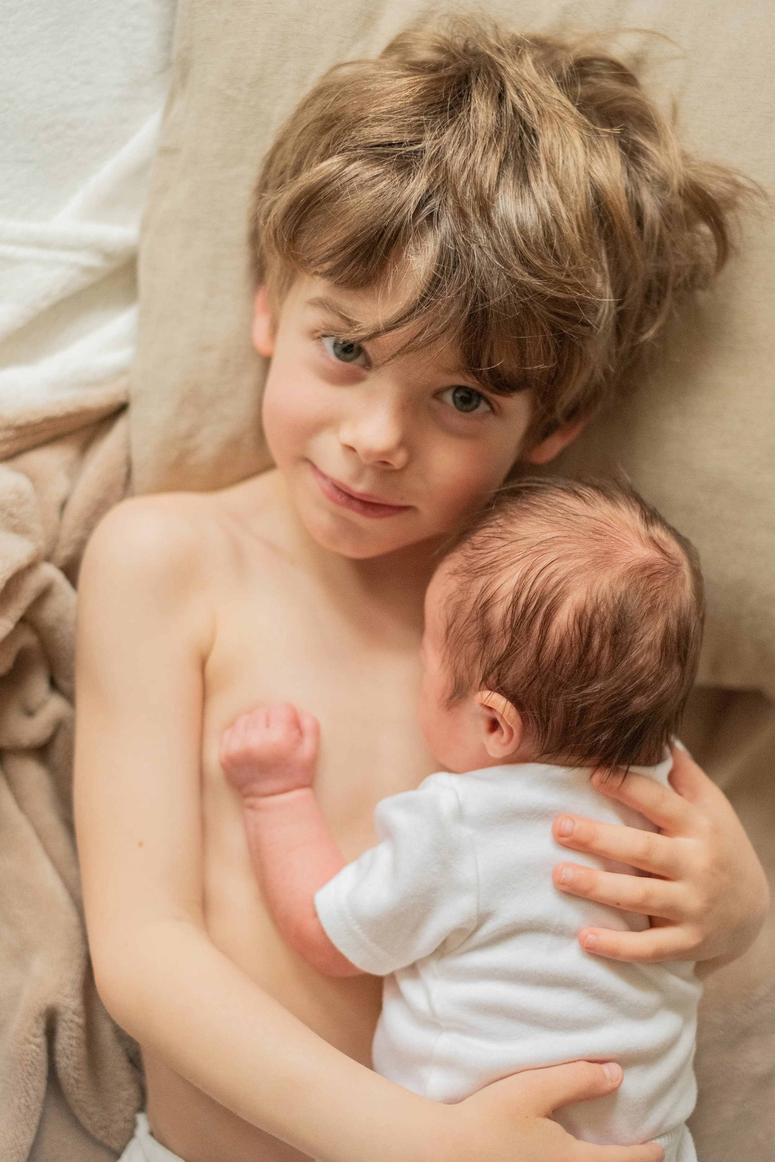 enfant allonge sur le dos avec son petit frere bebe sur son torse