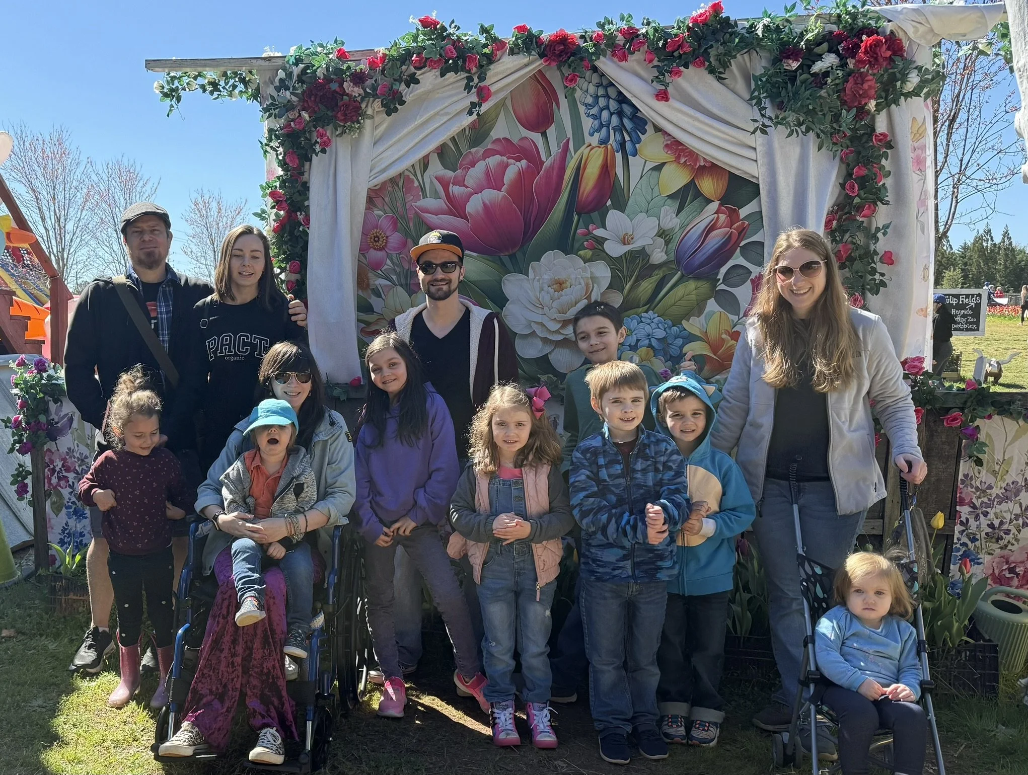 Beth Hovis's children and grandchildren gathered together outdoors for a family photograph in front of a colorful floral display.