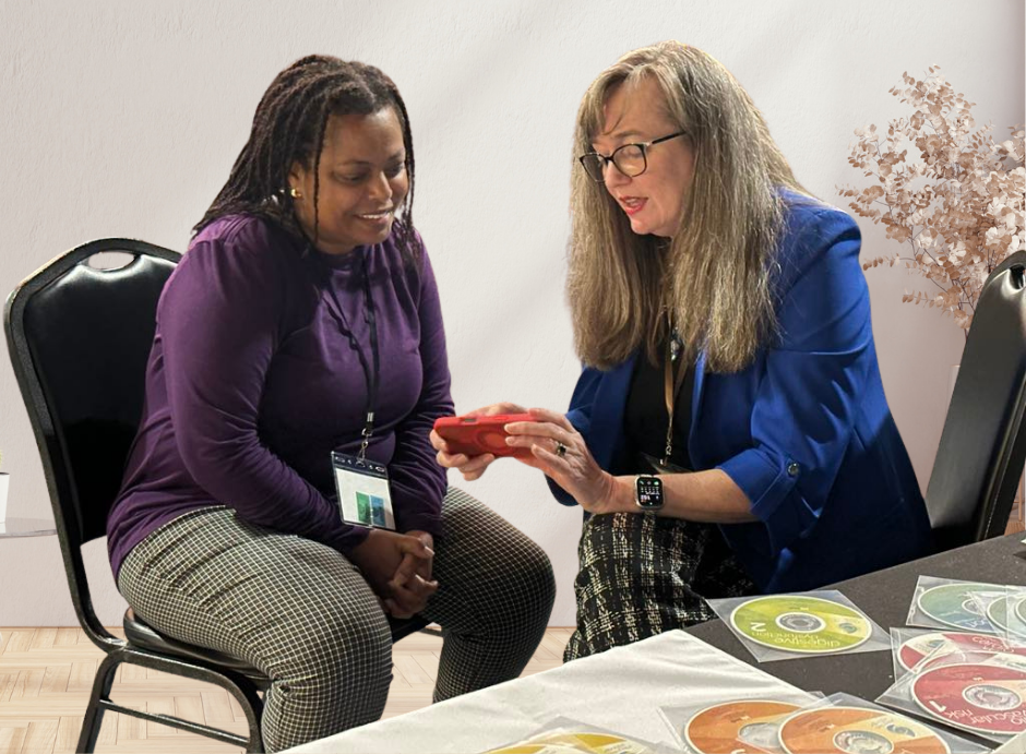 Beth Hovis sharing information on a smartphone with a woman seated beside her at an event table.