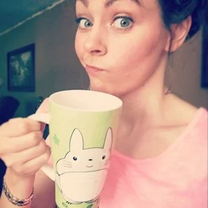Rebekah Bradley, contributor to holistic wellness and lifestyle blogs on BethHovis.com, holding a cup in a cozy indoor setting.