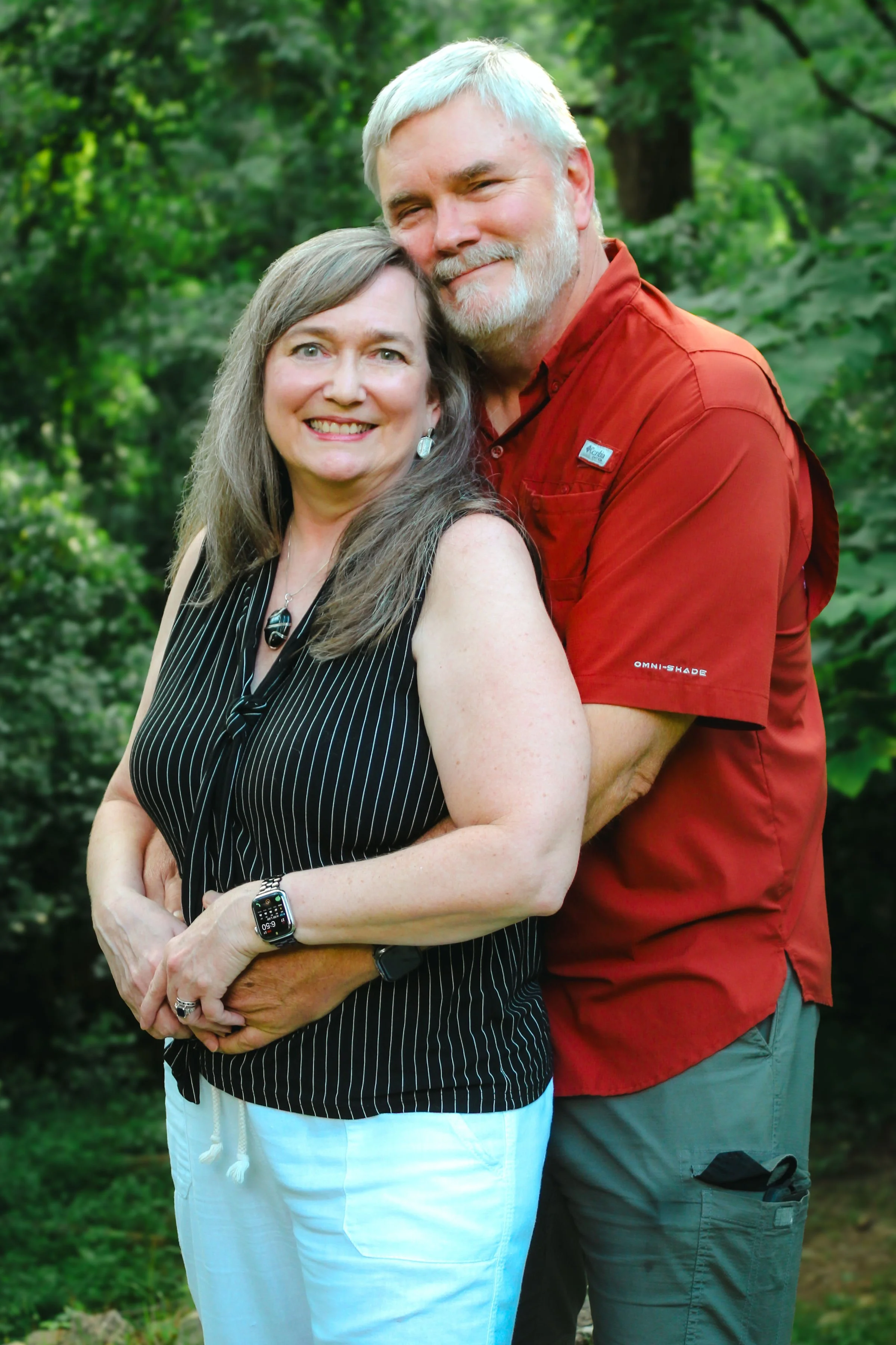 Beth Hovis and her husband, Rob, smiling together outdoors with greenery in the background.