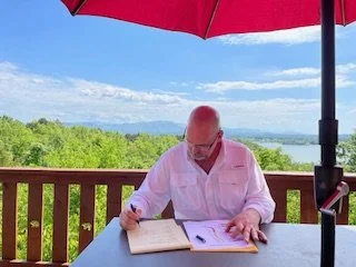 Participant reading and writing outdoors during a Brilliant Health Weekend Away with a scenic mountain and lake view.