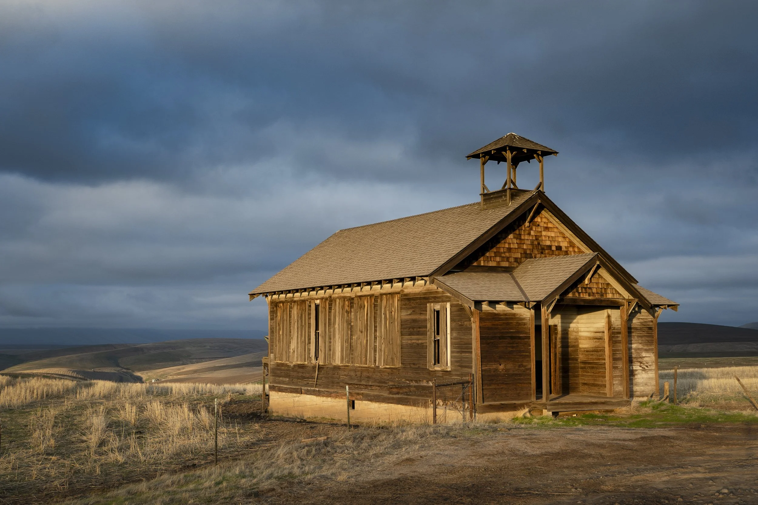 A wooden church with a steeple under a cloudy sky in a rural landscape.