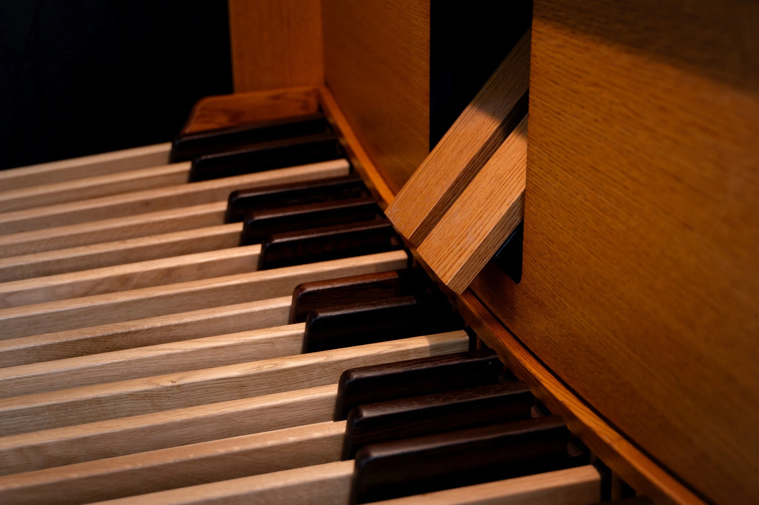 Close-up of a piano keyboard showing beige and black keys with a wooden piano body.