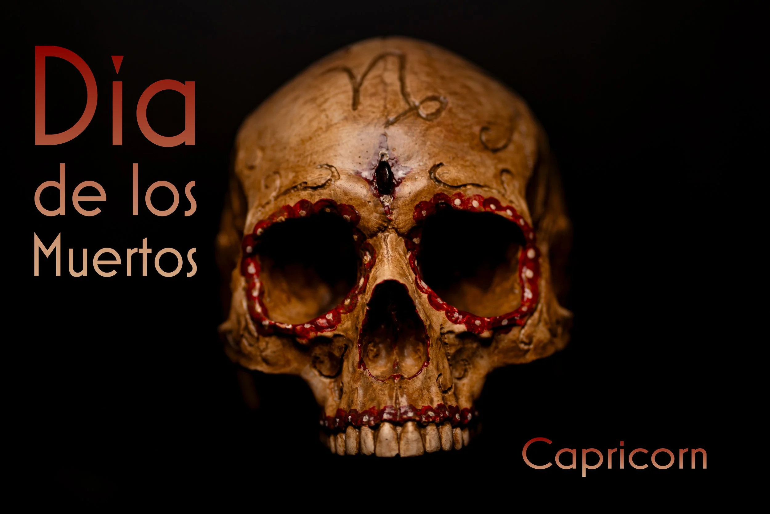 A human skull with red decorative accents around the eye sockets and teeth, set against a black background. Text on the left reads 'Día de los Muertos' in gradient shades of red and beige, and on the bottom right, 'Capricorn'.