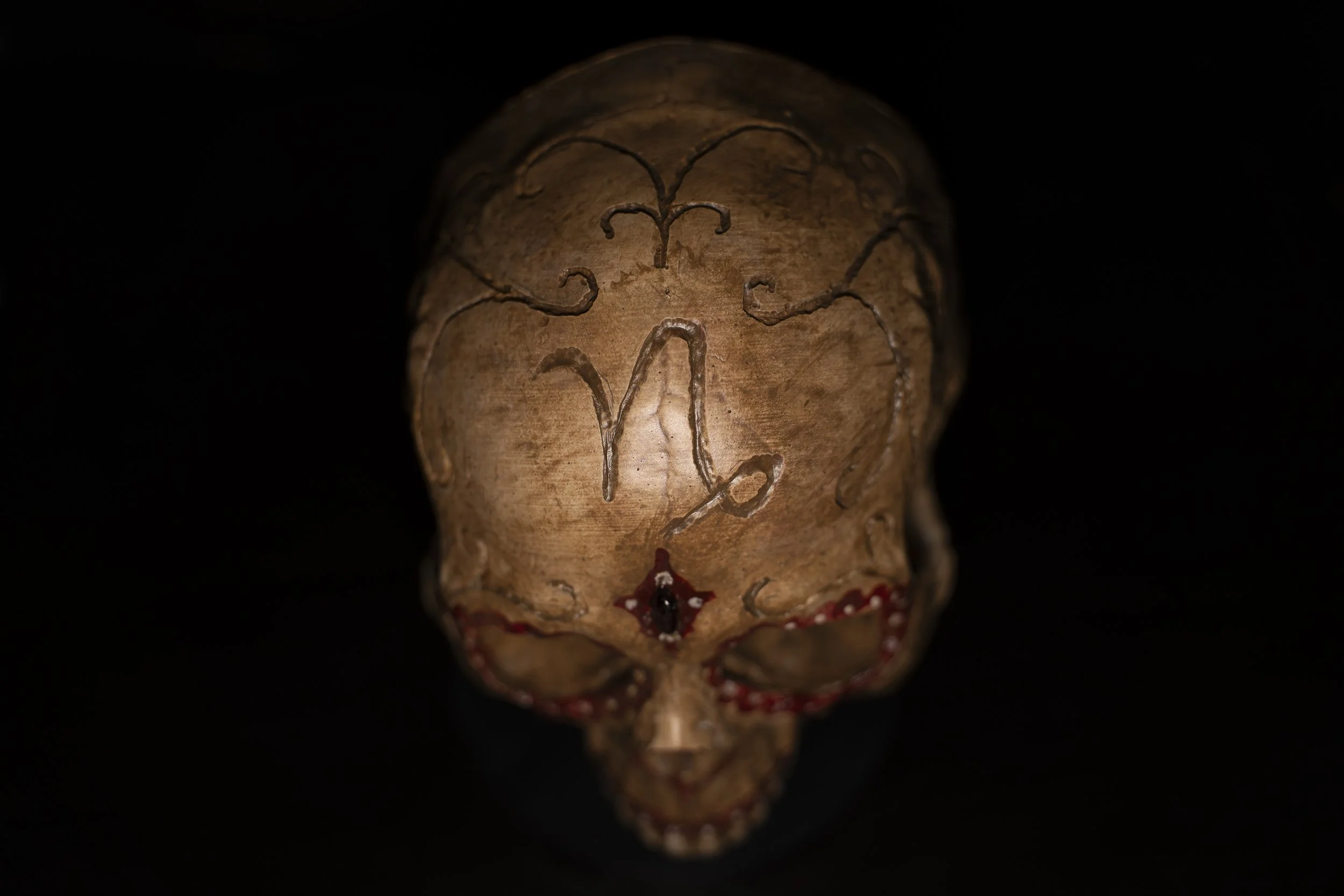 A decorated skull with carved designs and embellishments on the surface, set against a black background.