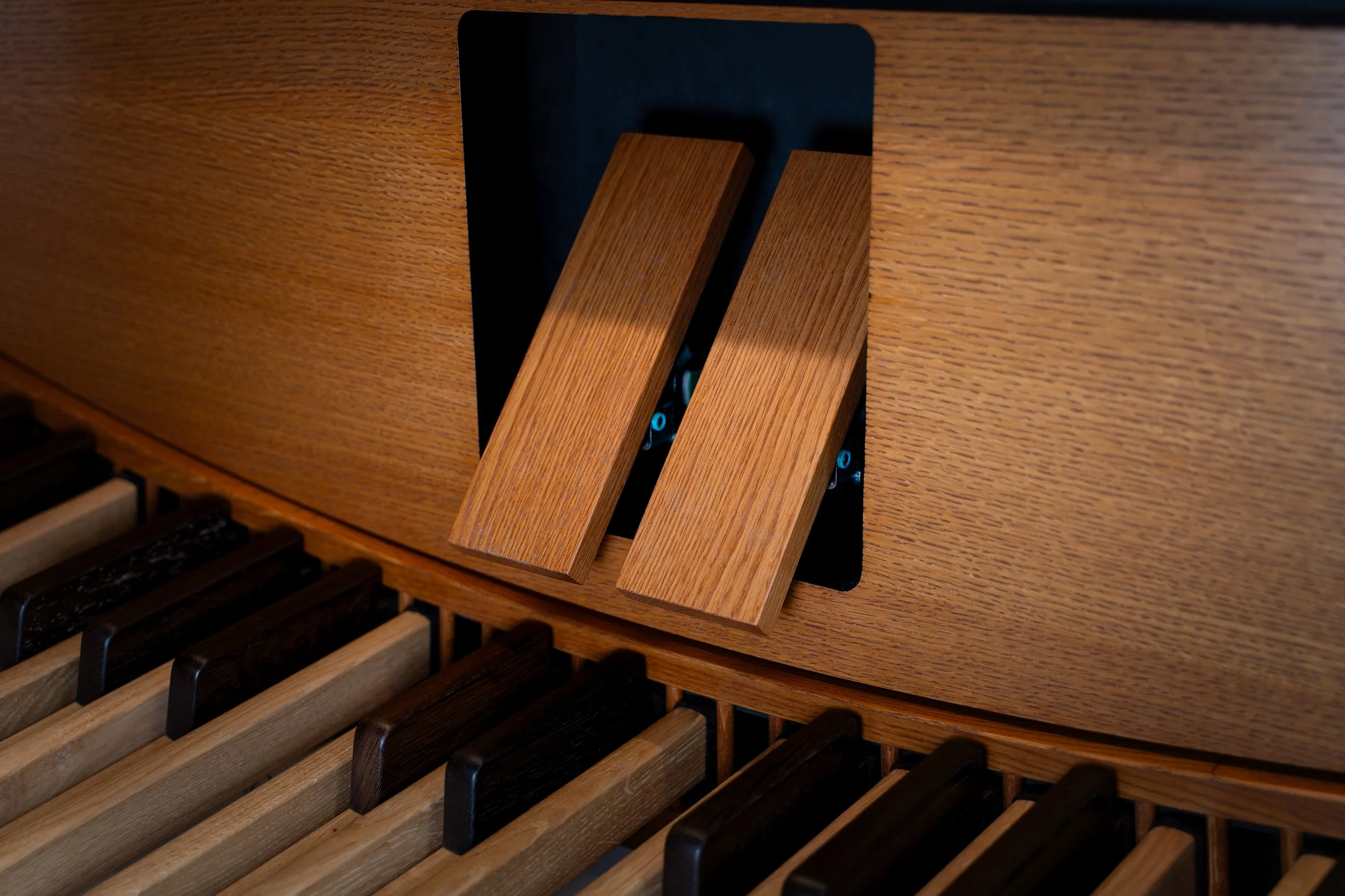 Close-up of a wooden piano keyboard with black and beige keys, and a wooden pedal switch opening in the piano's interior.