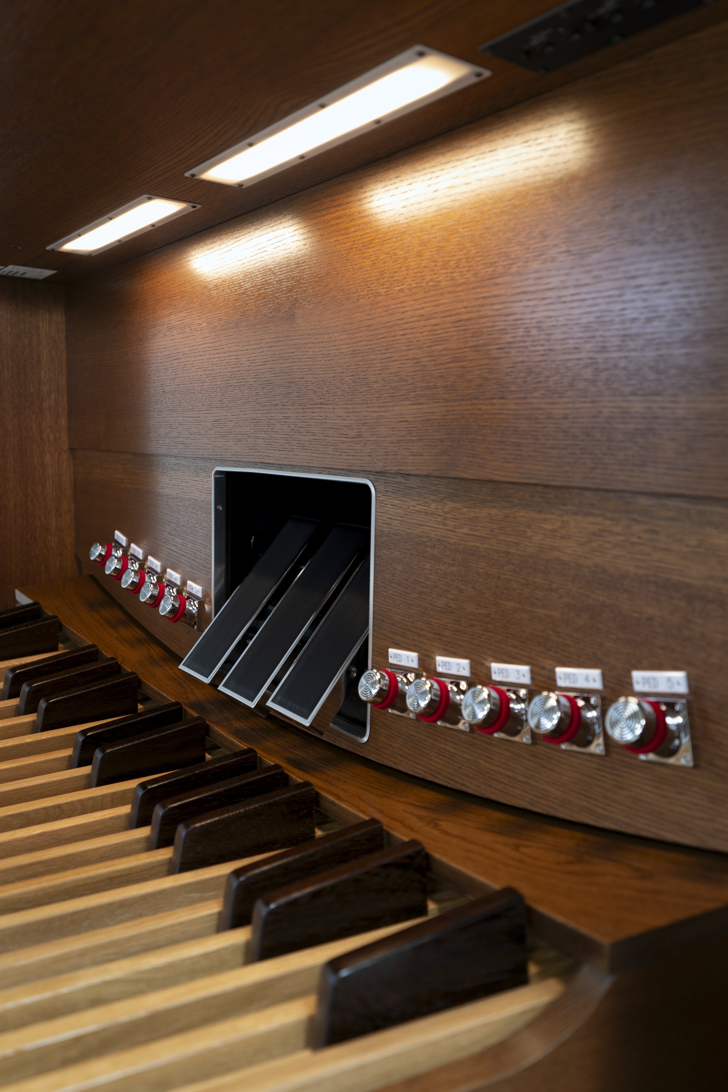 Close-up of a pipe organ keyboard with wooden keys and various electronic controls and stops above
