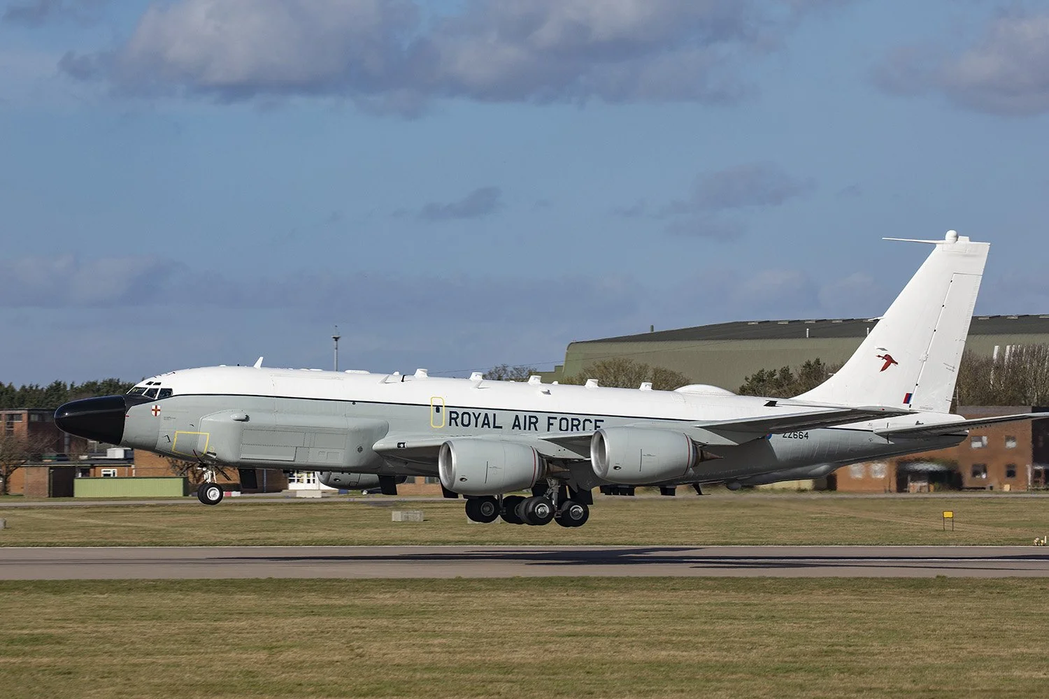 A Royal Air Force aircraft on the runway, painted in grey and white, with four engines, a large nose, and a distinctive tail fin with a red emblem.