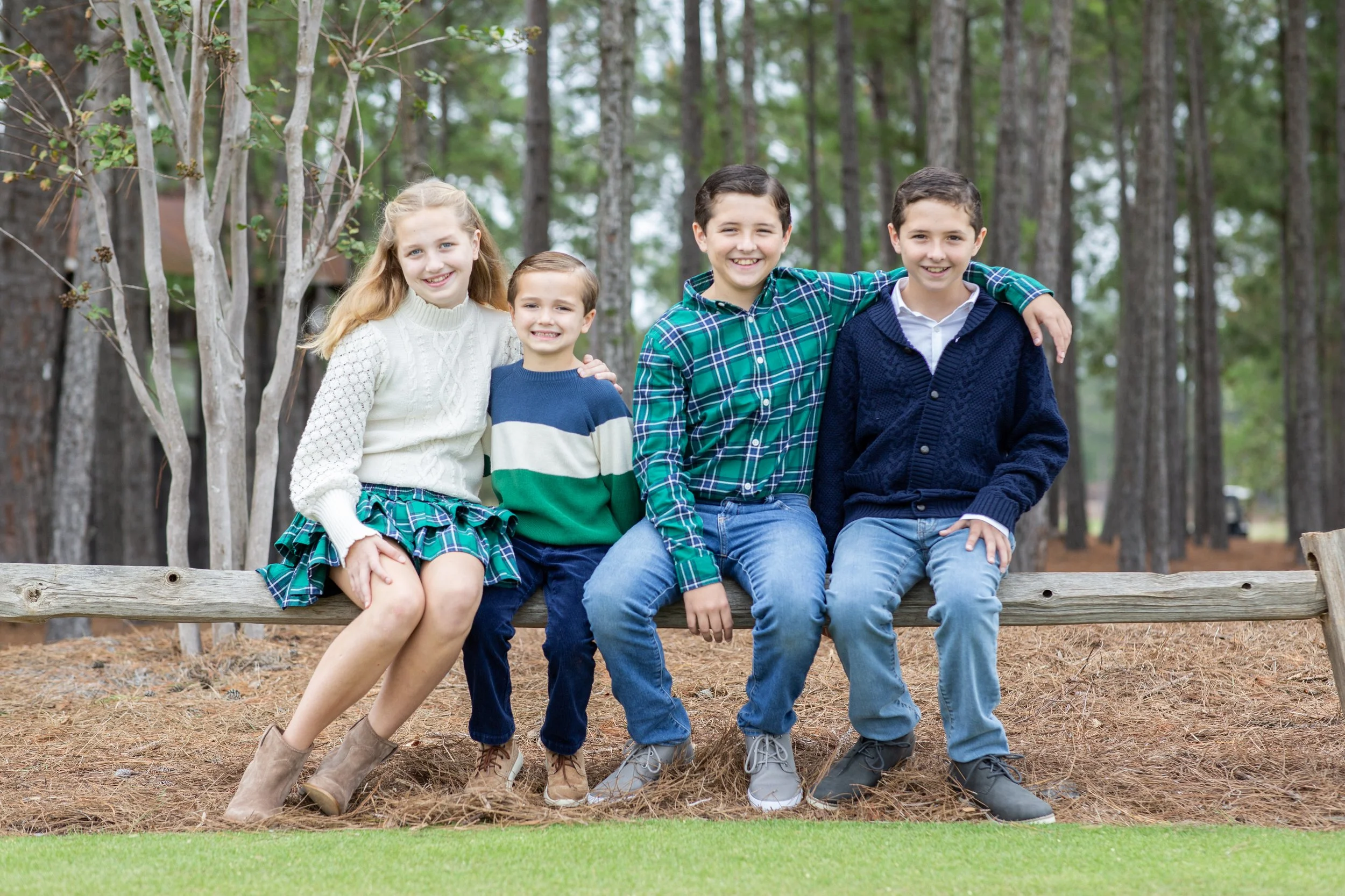 Five children sitting on a wooden bench outdoors in a wooded area, smiling at the camera. Photographed by Houston Photographer Katie Park.