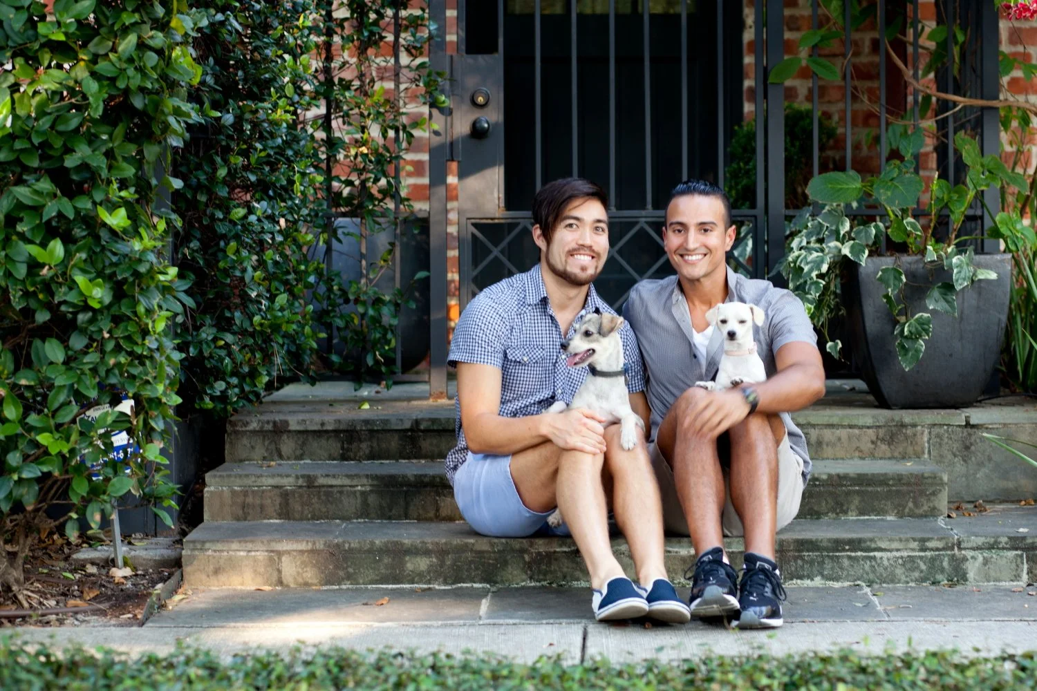 Two men sitting on stairs outside with two dogs, surrounded by plants. Photographed by Houston Photographer Katie Park.