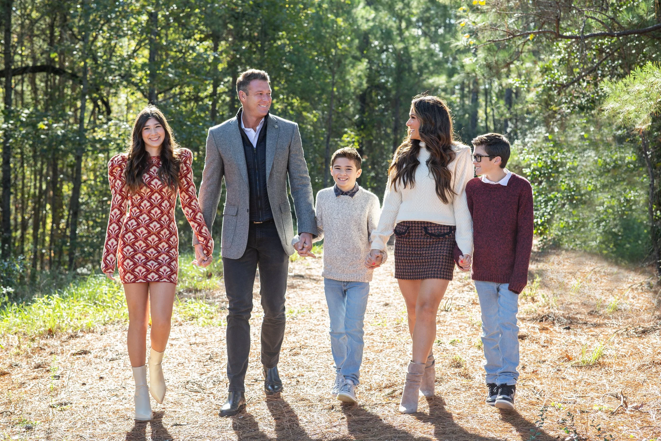 A family of six walking hand in hand through a forest during daytime, smiling and enjoying each other's company. Photographed by Houston Photographer Katie Park.