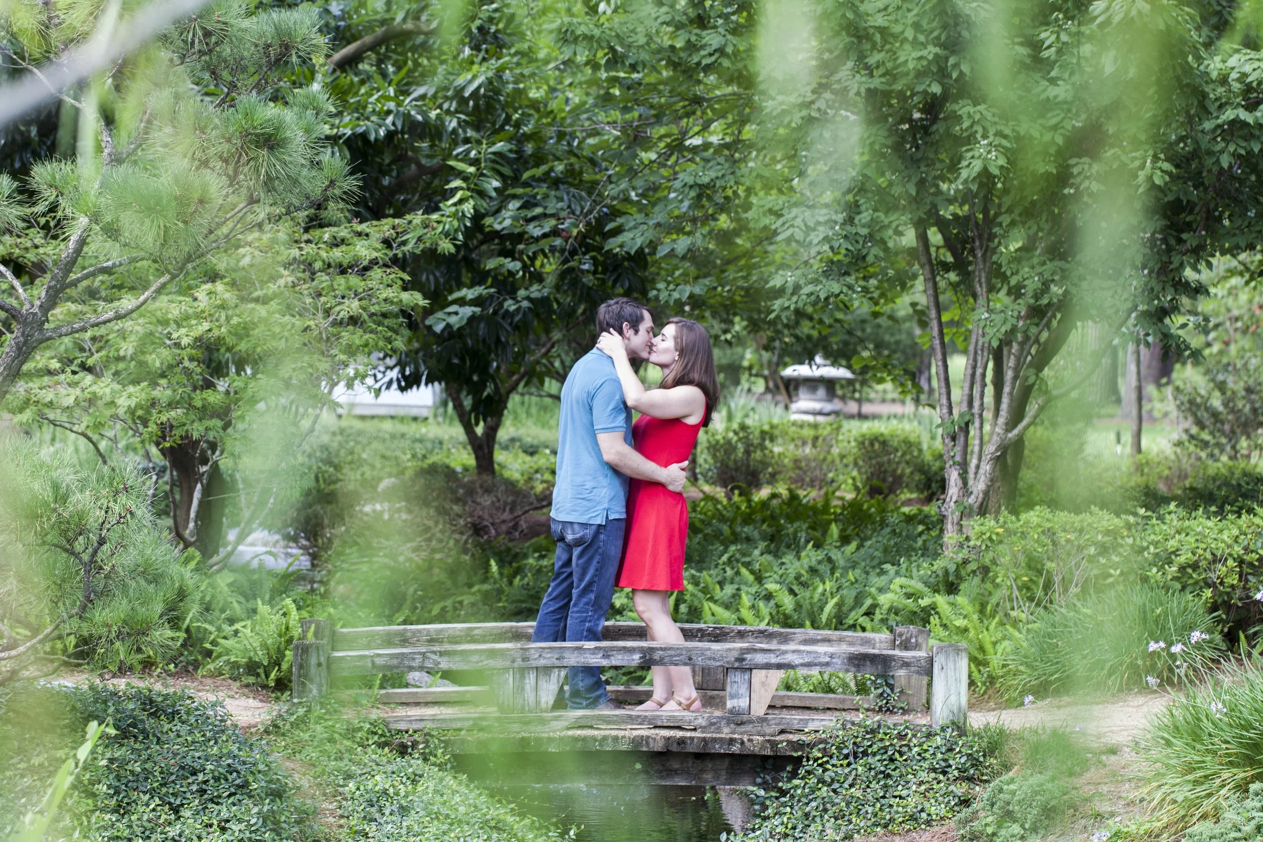 A couple sharing a kiss on a small wooden bridge in a lush green garden.