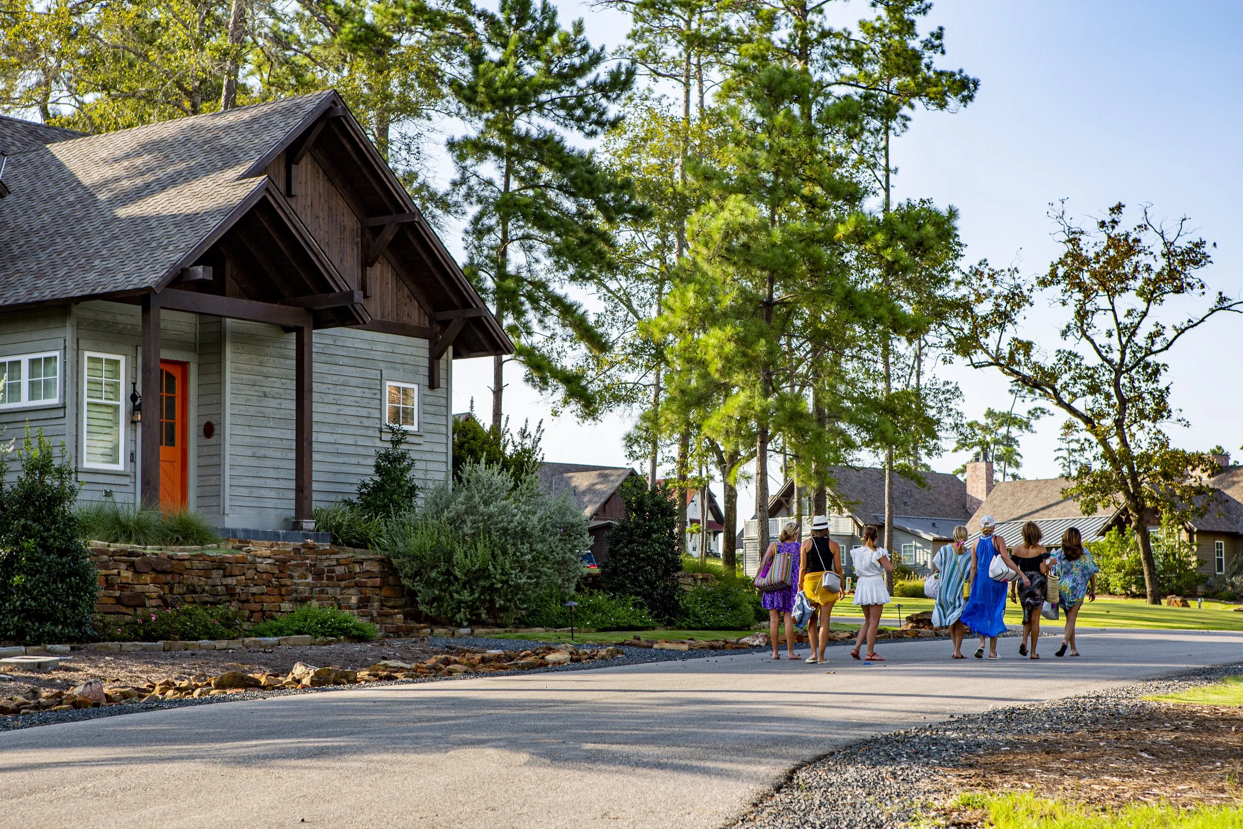 Group of women walking on a neighborhood sidewalk surrounded by trees and houses during daytime.