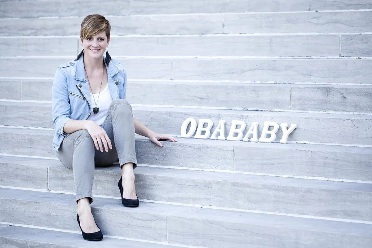 A woman with short hair sitting on a staircase next to white 3D letters spelling 'OBABY.'