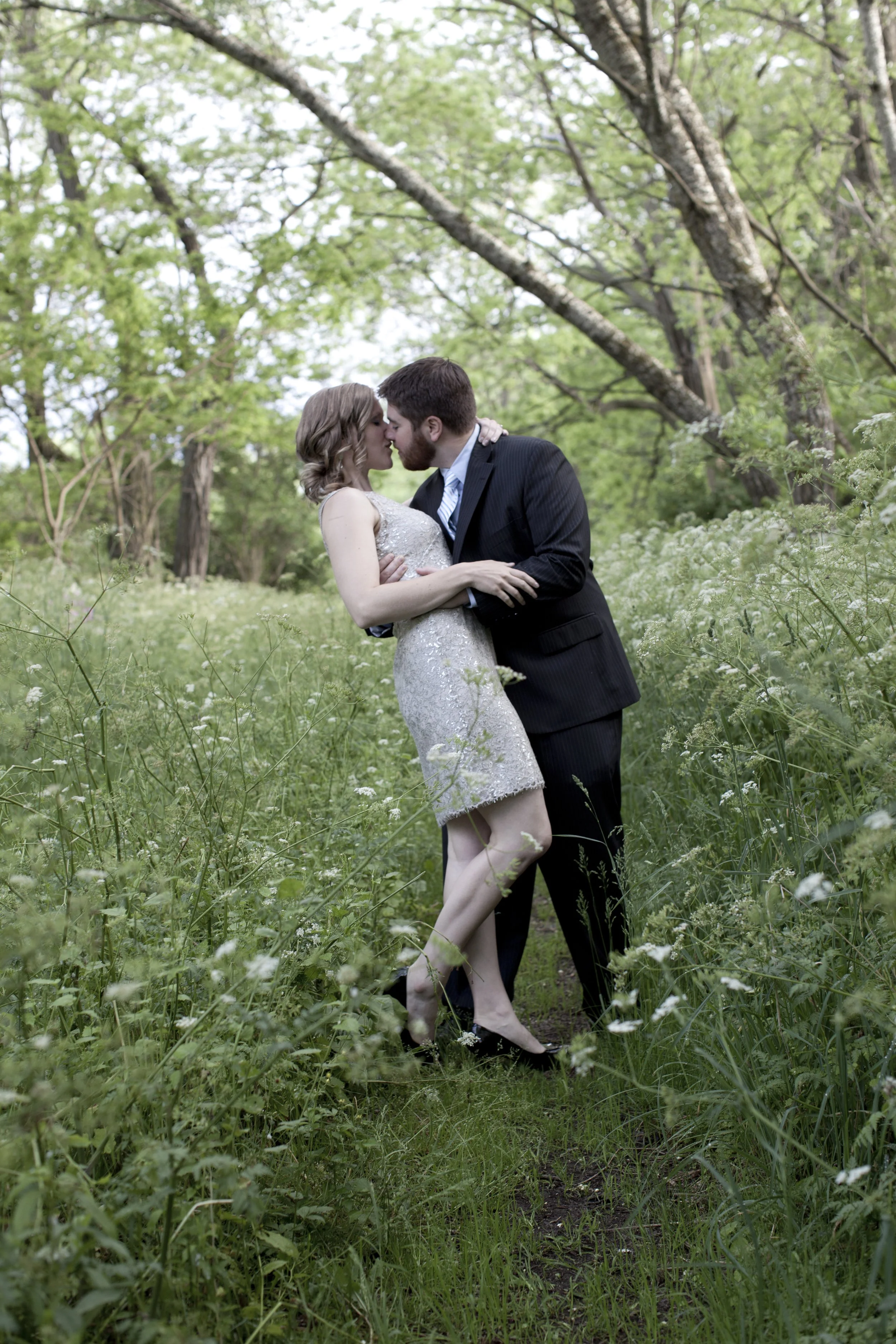 A man and woman kiss in a lush, green, wooded outdoor setting. Photographed by Houston Photographer Katie Park.