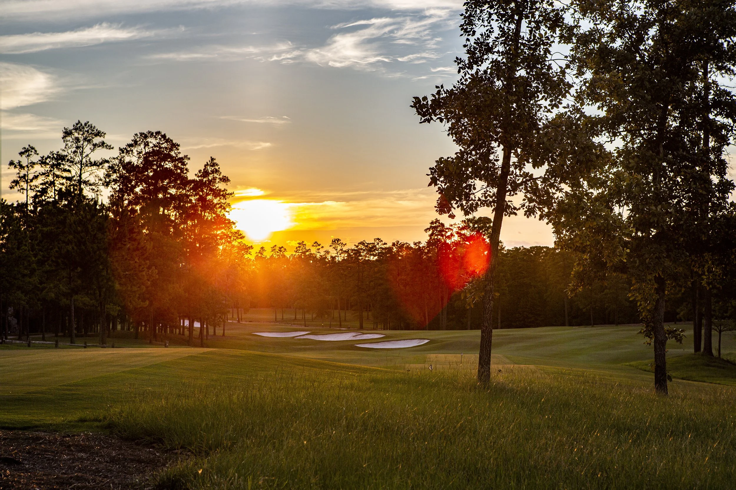 Sunset over a golf course with trees and sand bunkers.