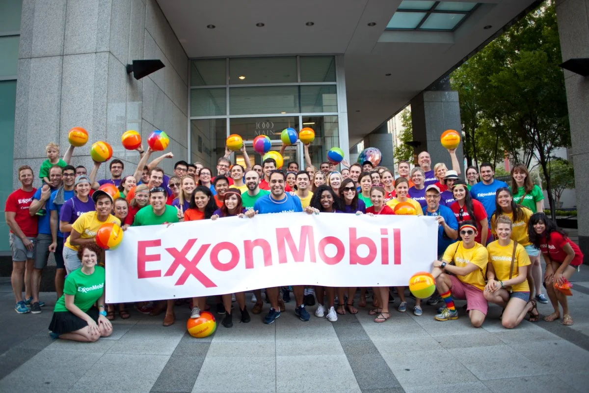 Group of people holding an ExxonMobil banner outside a building, some holding colorful beach balls, smiling and posing for a photo.