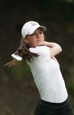 Person wearing a white cap and shirt swinging a golf club outdoors.