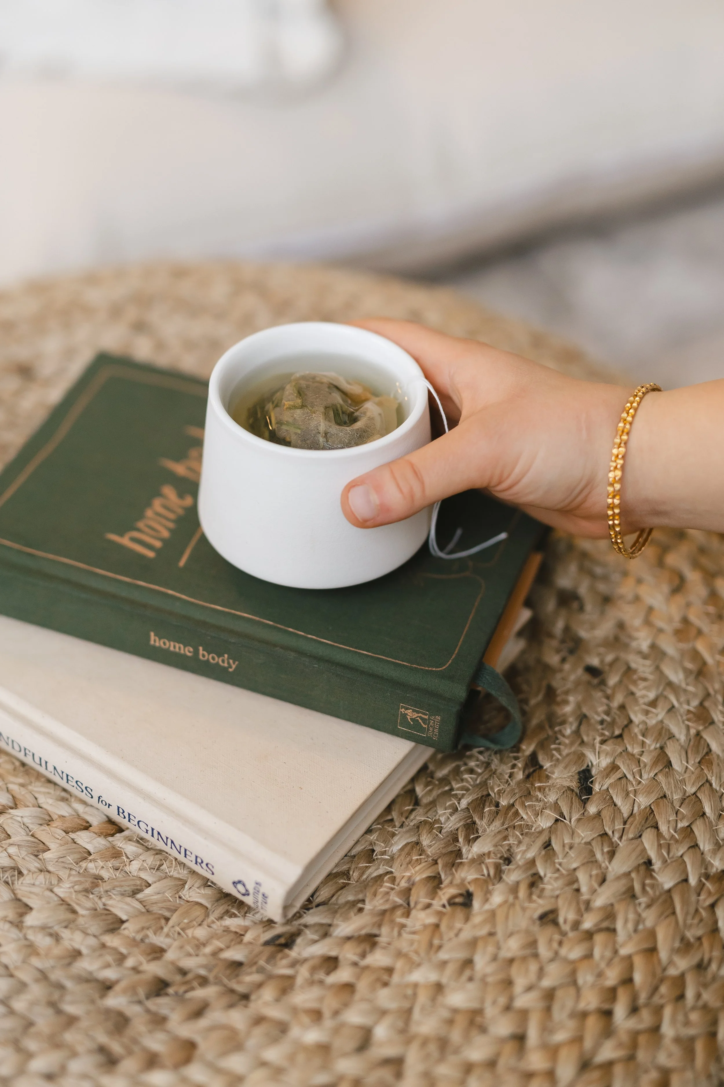 close up of a hand holding a cup of tea on a stack of 2 books | &asanas hot yoga and pilates studio in london, ontario