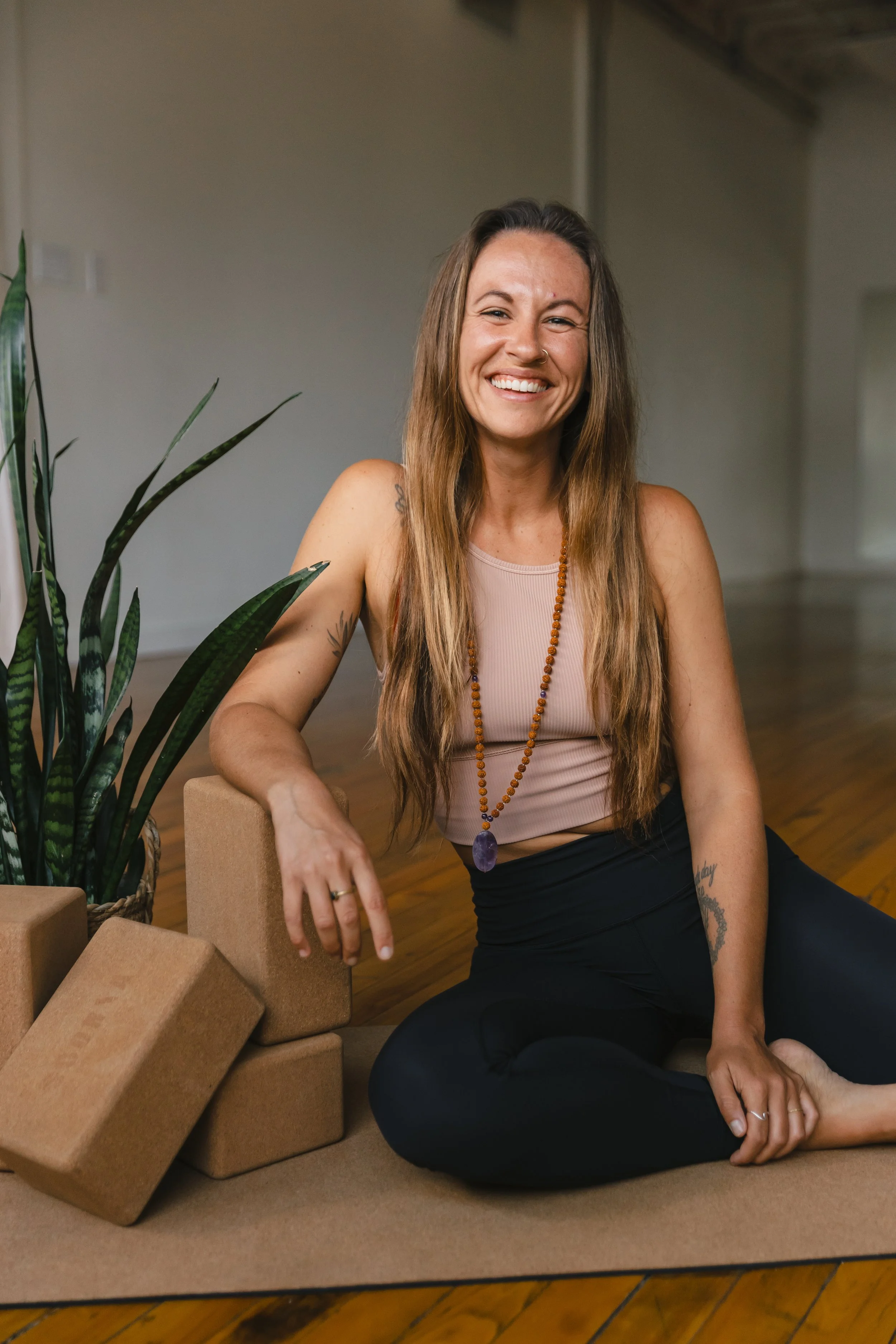 emily cordes sitting on the ground smiling | &asanas hot yoga and pilates studio in london, ontario