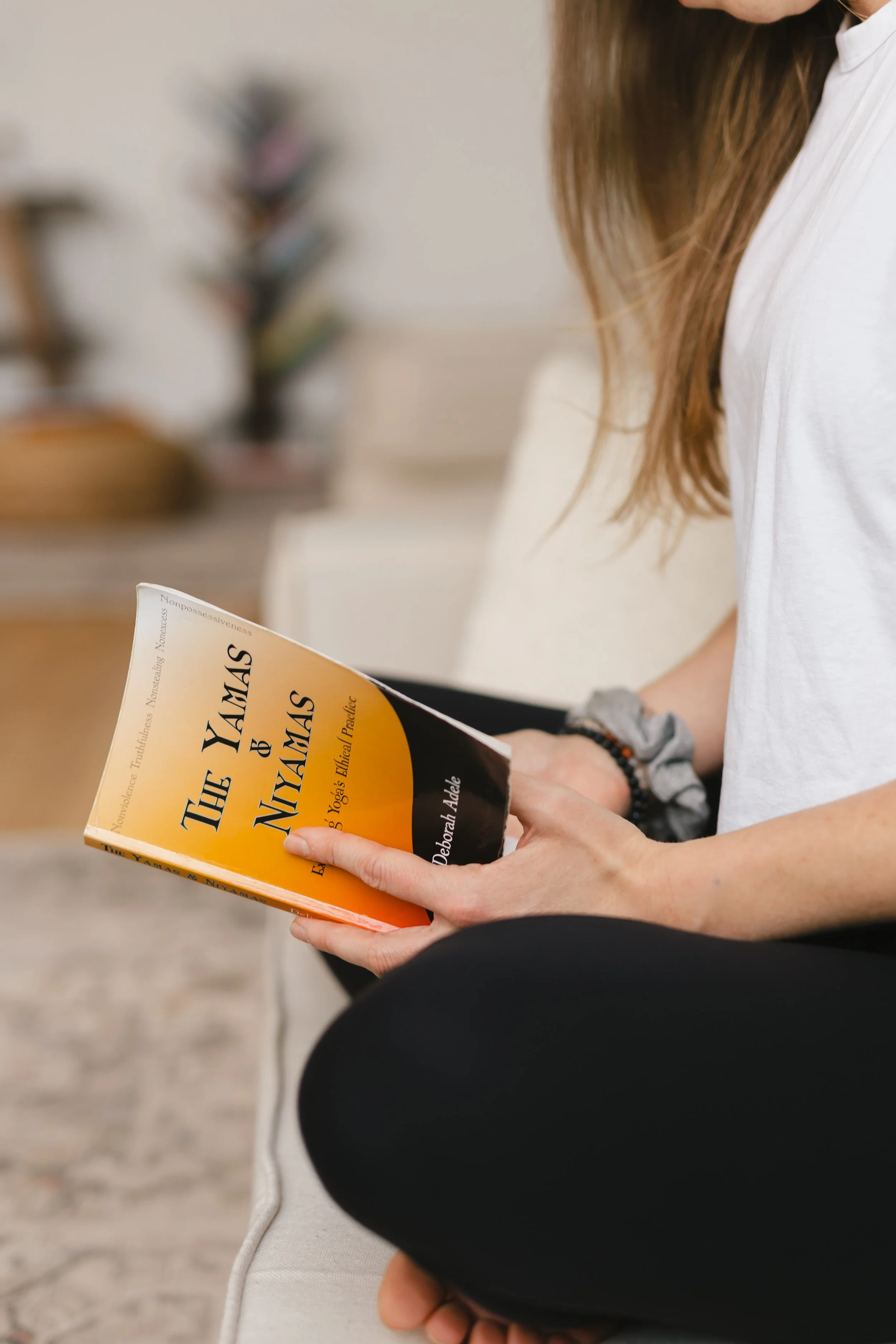 a woman close up holding and reading a book called "the yamas and niyamas" while sitting on the floor in a yoga studio | &asanas hot yoga and pilates studio in london, ontario