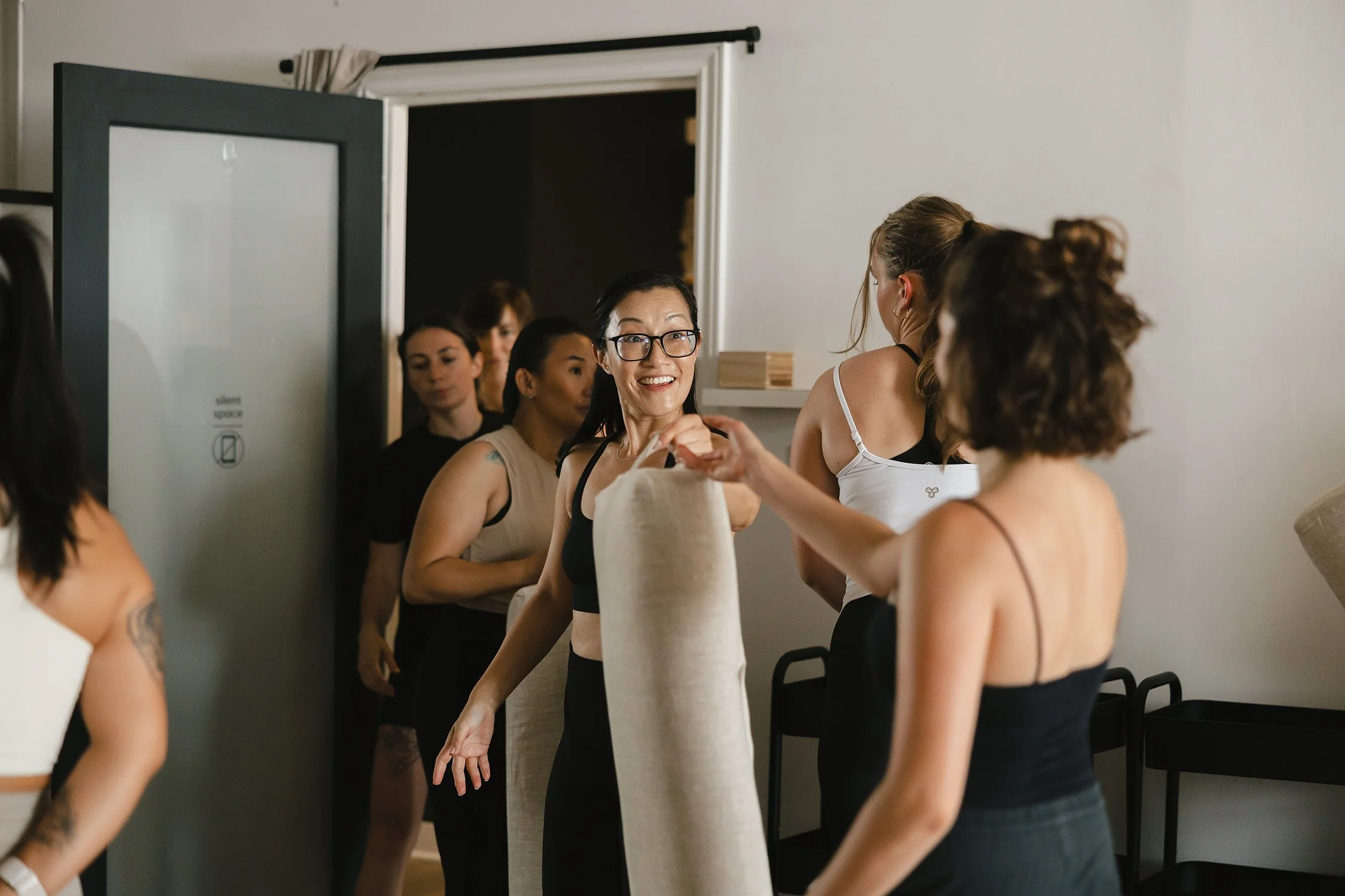 woman helping each other pack up yoga equipment | &asanas hot yoga and pilates