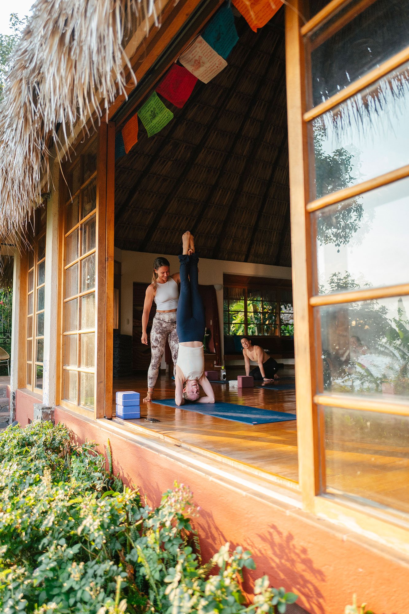 A woman holding the legs of another person who is doing a headstand in a yoga pose