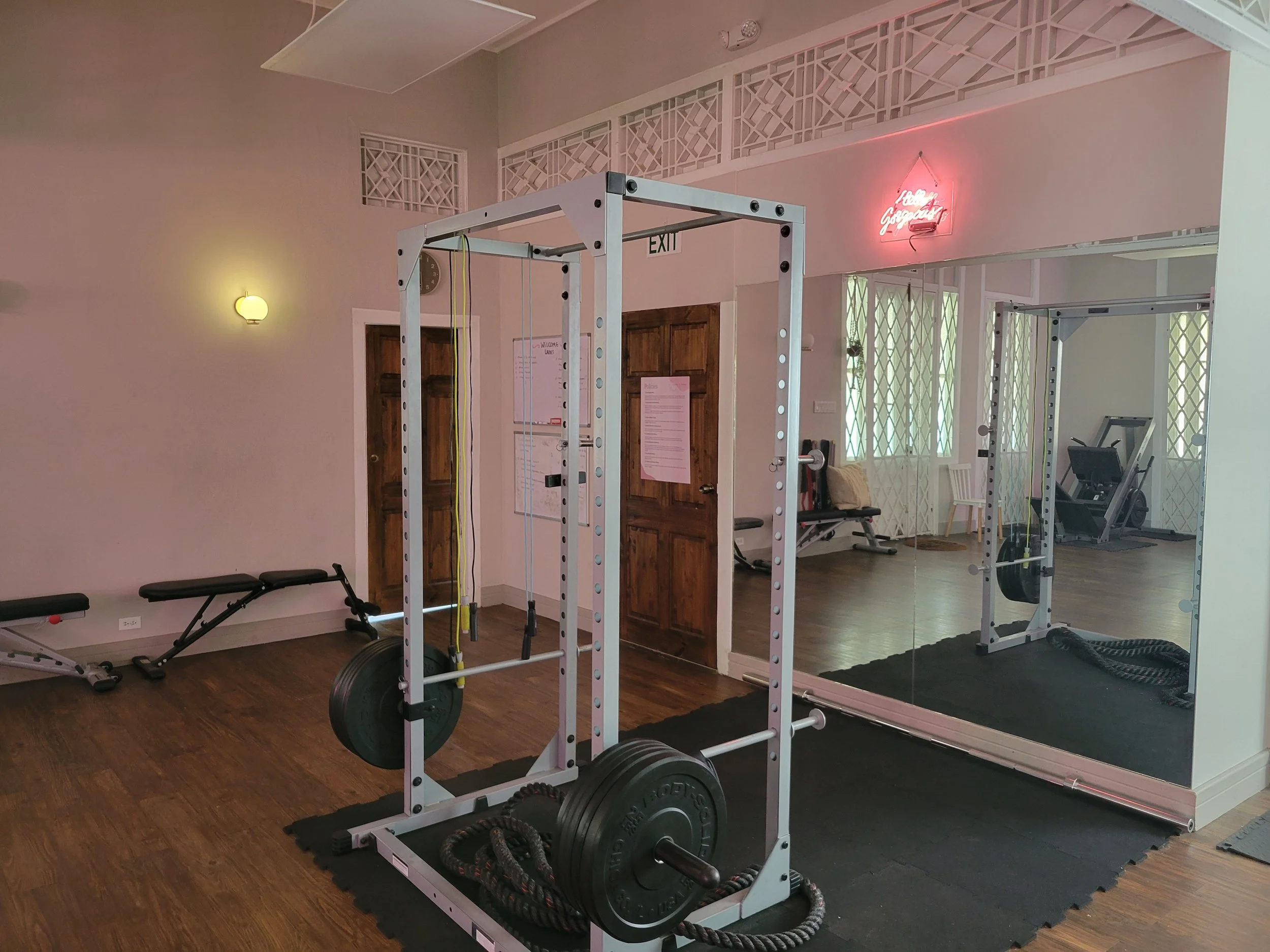 Gym with weightlifting equipment, resistance bands, mirror, bench, and a neon sign that reads 'Happy Goggans' on the wall.