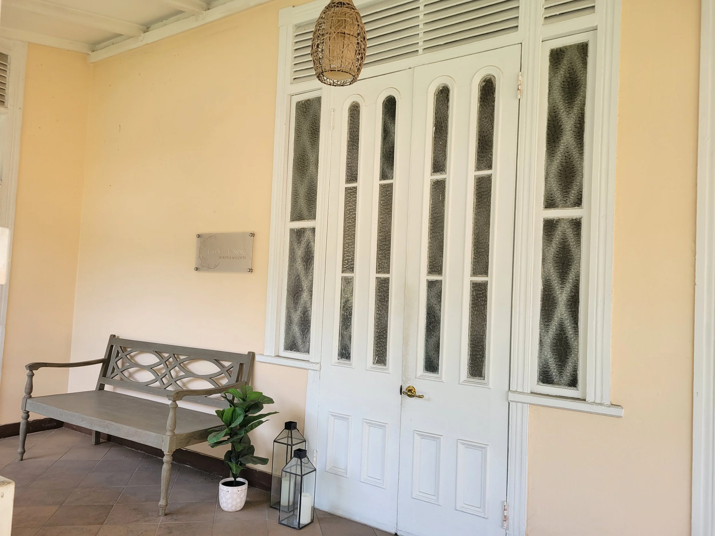 Front porch with a white door and decorative glass windows, a wooden bench, a potted plant, and lanterns.