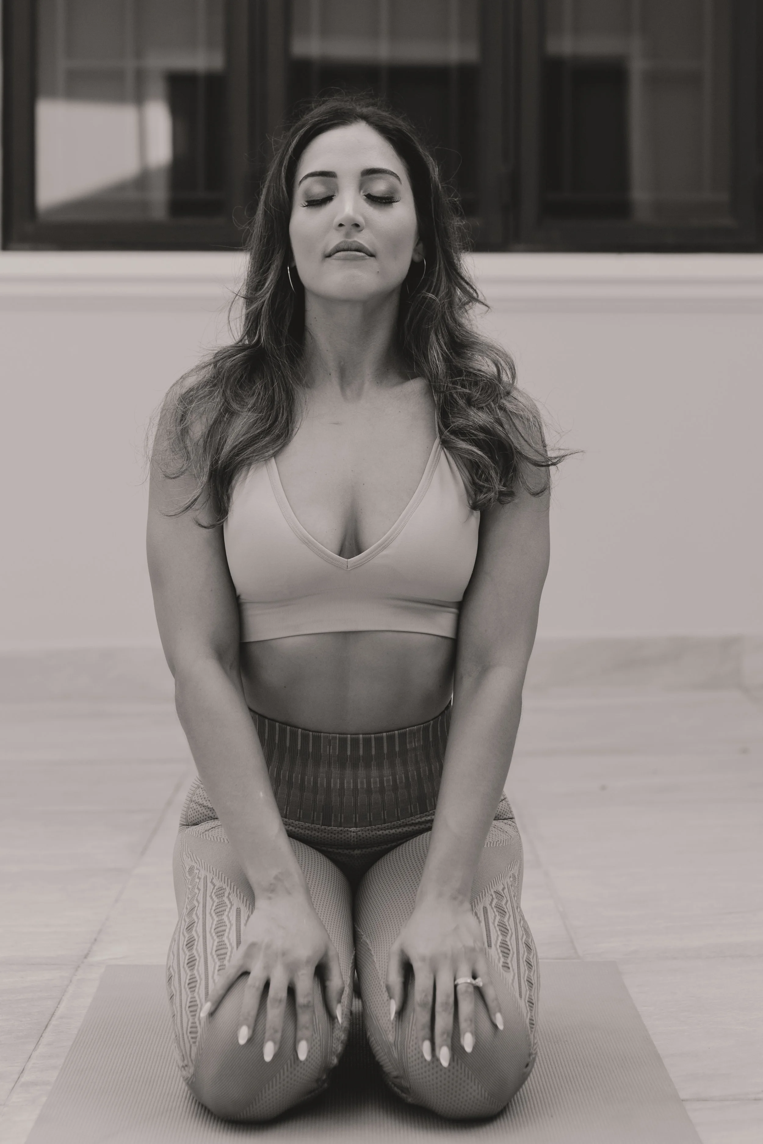 A woman practicing yoga or meditation in a seated kneeling position with eyes closed, indoors.
