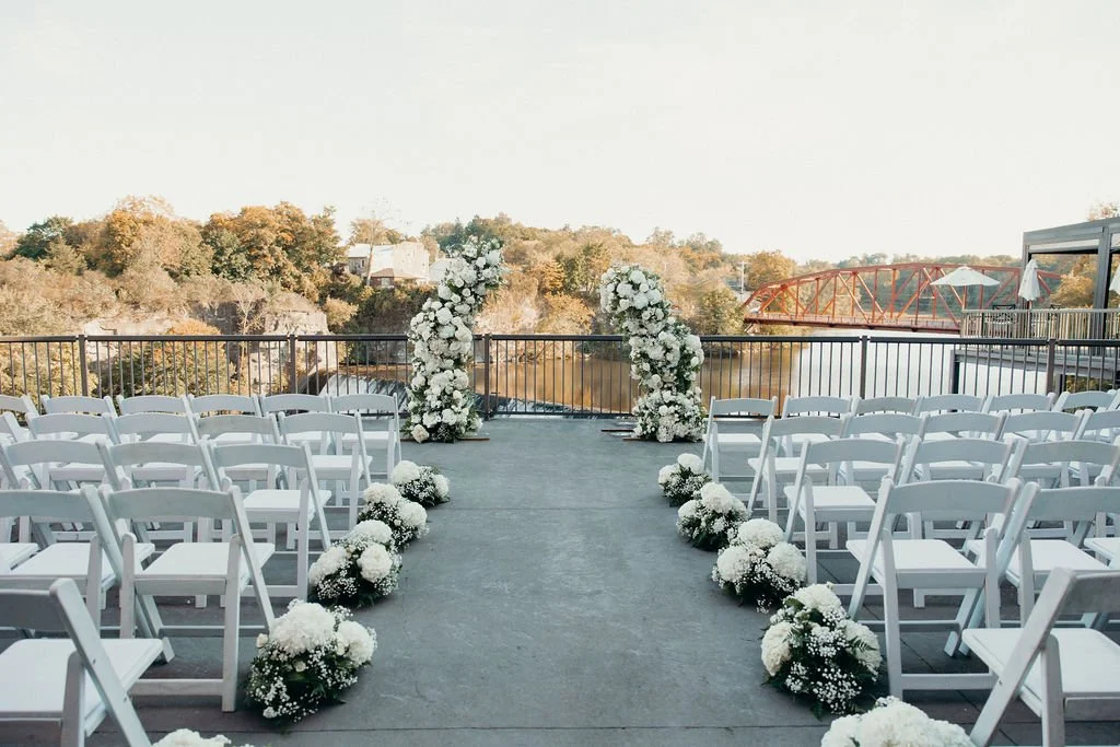 Riverside wedding ceremony setup with white chairs and floral altar arrangements at Diamond Mills Hotel