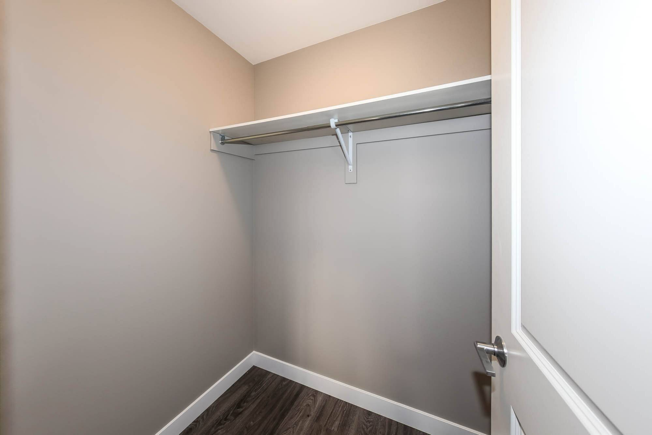 Empty walk-in closet with beige walls, white shelf, and rod for hanging clothes.