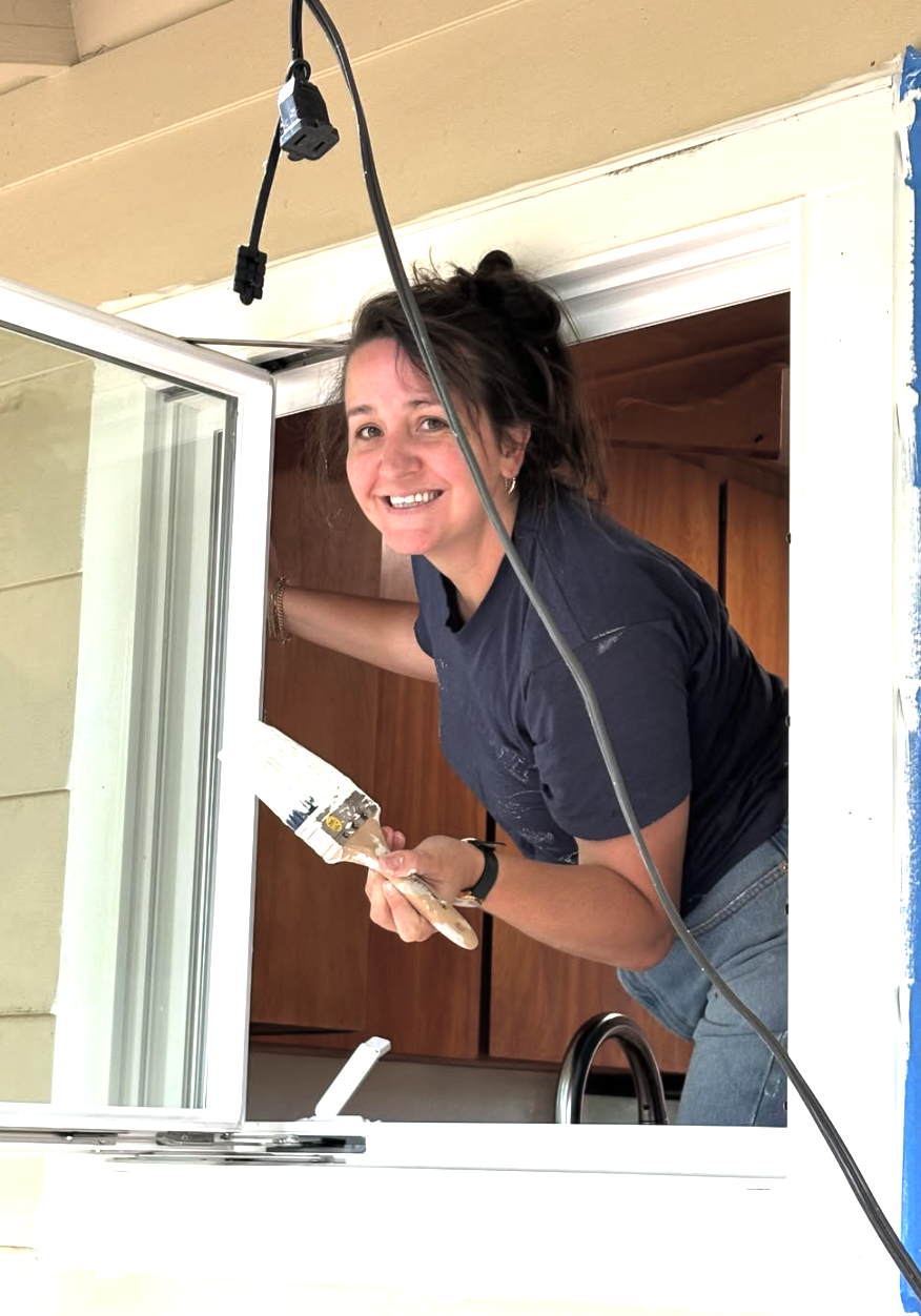 Woman painting window frame inside a house, smiling
