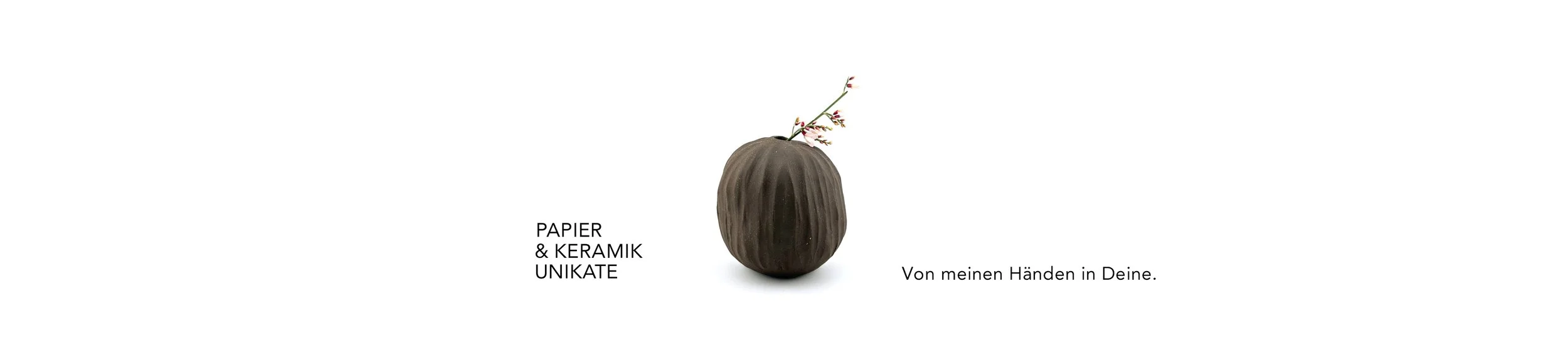 Ein Keramikgefäß mit kleinen Zweigen und Blüten. Text in Deutsch: "Papier & Keramik Unikate. Von meinen Händen in Deine."