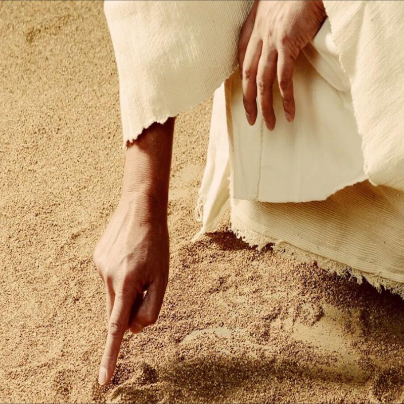 A figure in a white robe traces shapes in the sand