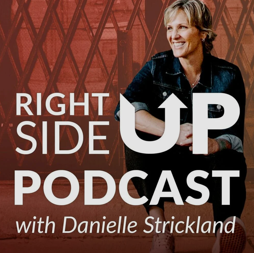 Danielle Strickland sits on the sidewalk curb and looks off to the left, smiling.
