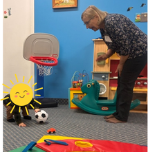 A nursery minister watches over a young child who is playing with a soccer ball.