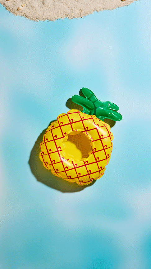 a stop motion of a pineapple floaty moving across a fake water backdrop with a piece of toast and peanut butter with the money sign made out of honey on top floating onto a beach with umbrellas and palm trees