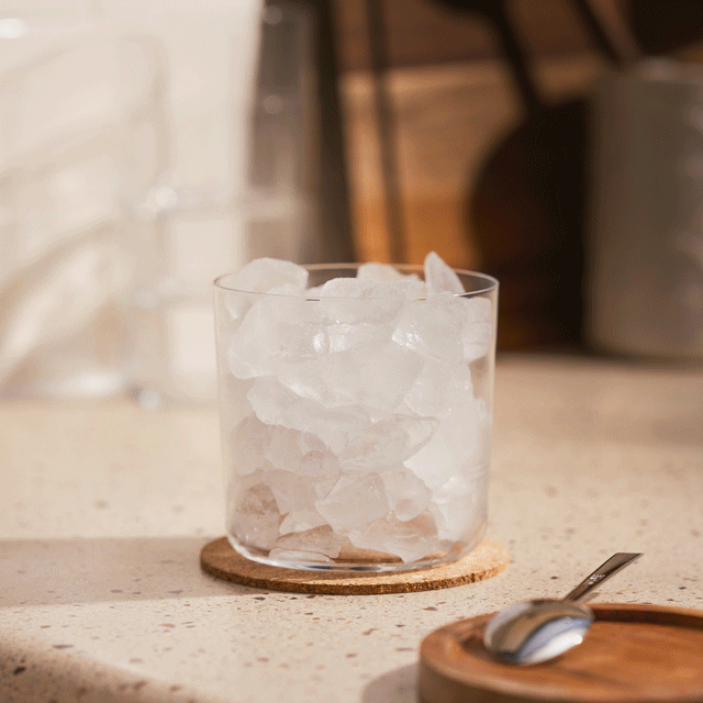 a stop motion of a single glass resting on a cork coaster on a countertop, glass is filled with ice and then is filled with coffee, milk so you can see the milk swirl and then the hand removes it from the frame