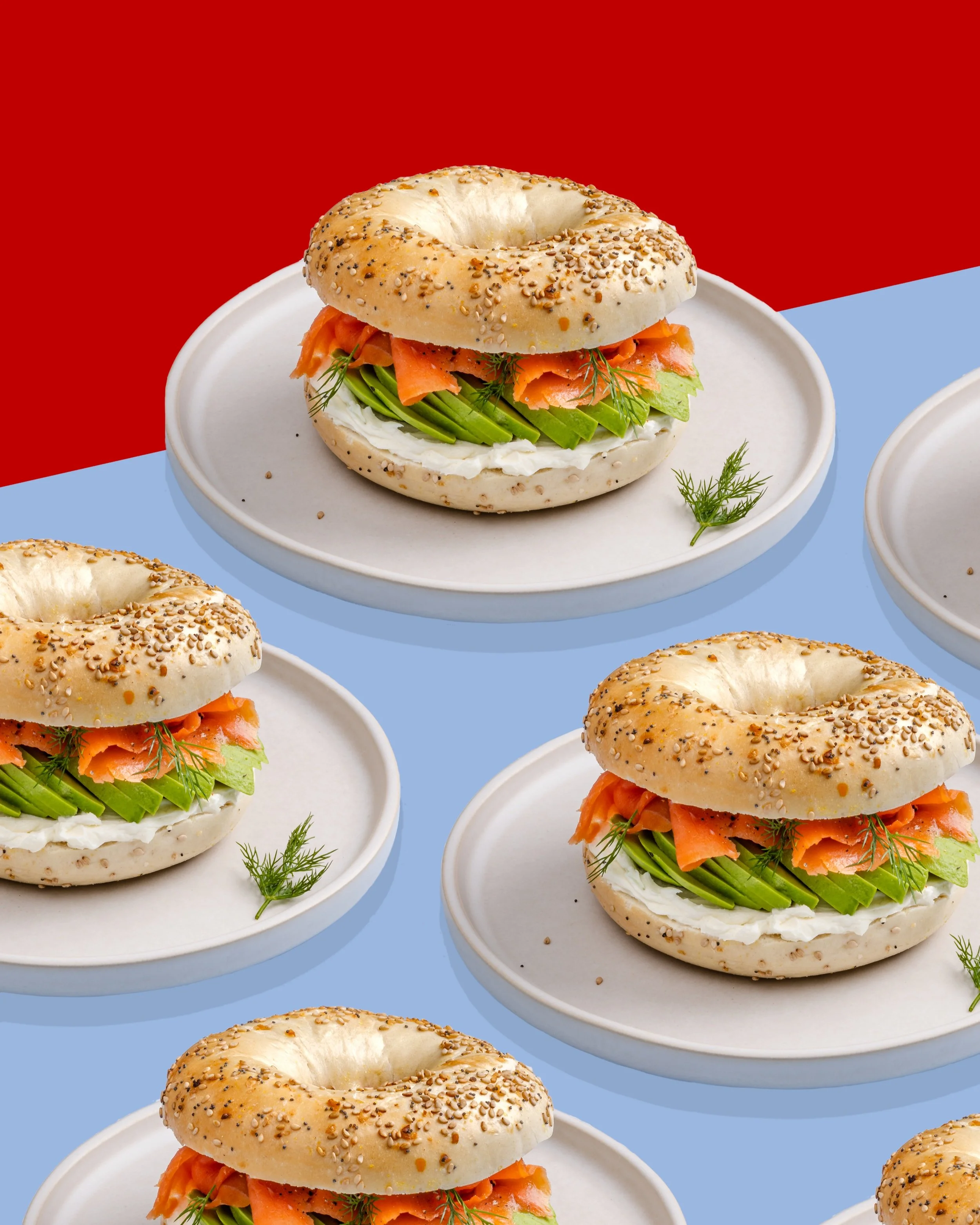salmon lox and avocado bagels on a plate creating a pattern with a blue and red background