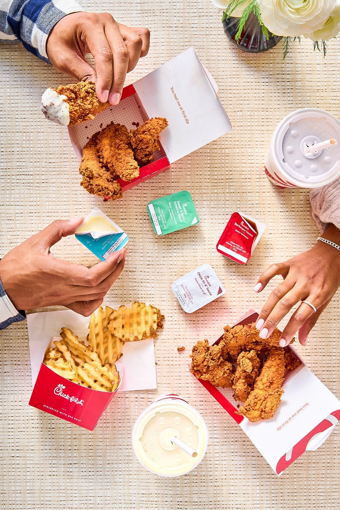 overhead scene at chick-fil-a canada restaurant with a man and woman holding the crispy chicken tenders and the waffle fries with a variety of sauces in the frame