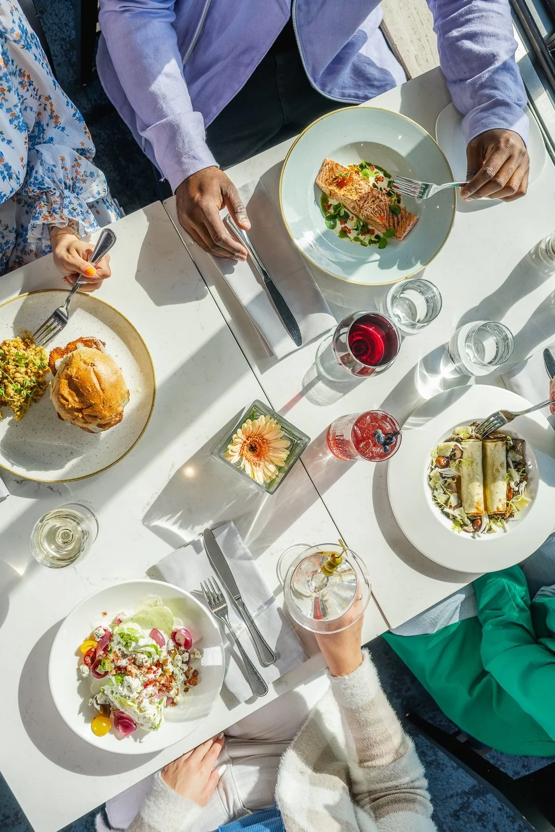 overhead tablescene of plates of food and people reaching to grab drinks or forks