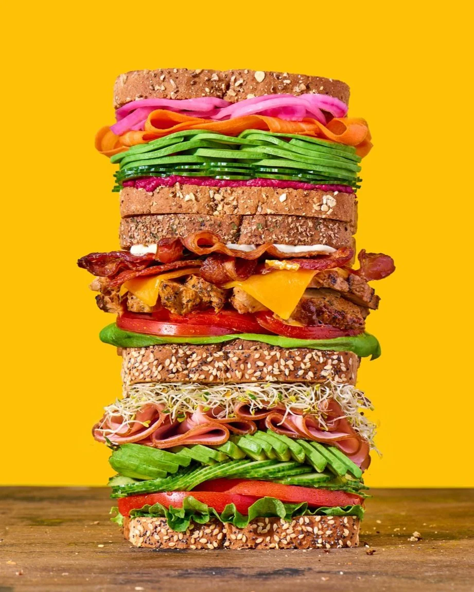 sandwich stack with fresh veggies, bacon, chicken, on a wooden surface