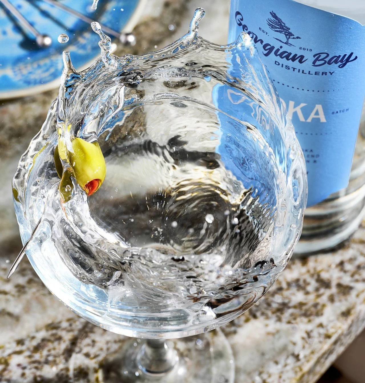 a martini with a vodka bottle behind and an olive making a splash
