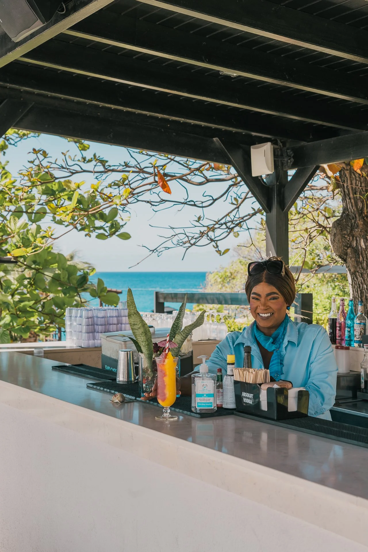 a woman smiling at an outdoor bar area at a resort with the ocean in the background
