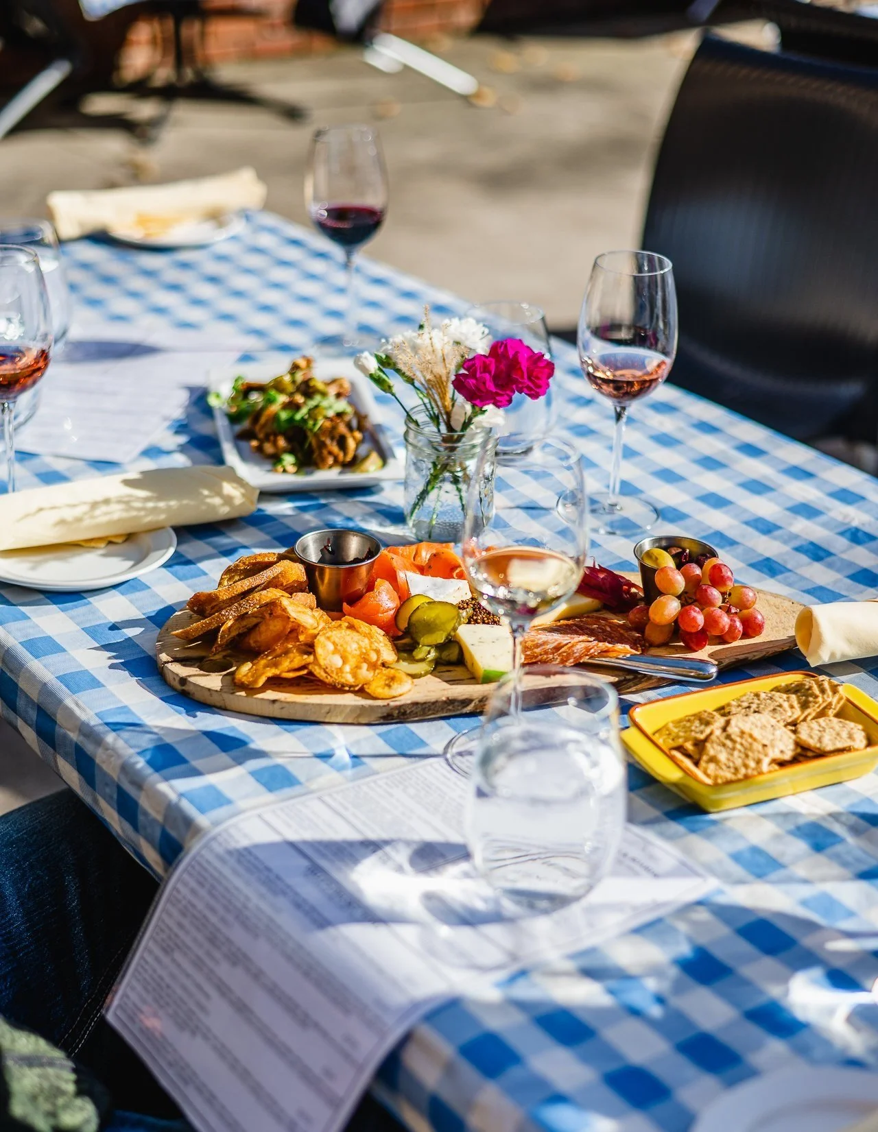 platter with crackers and grapes and wine glasses on a blue and white checkered table outside