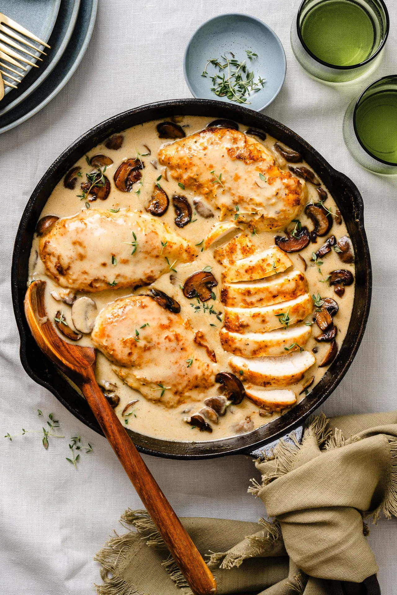 overhead shot of a chicken and mushroom dish in a cast iron pan with glasses and plates beside it on a table