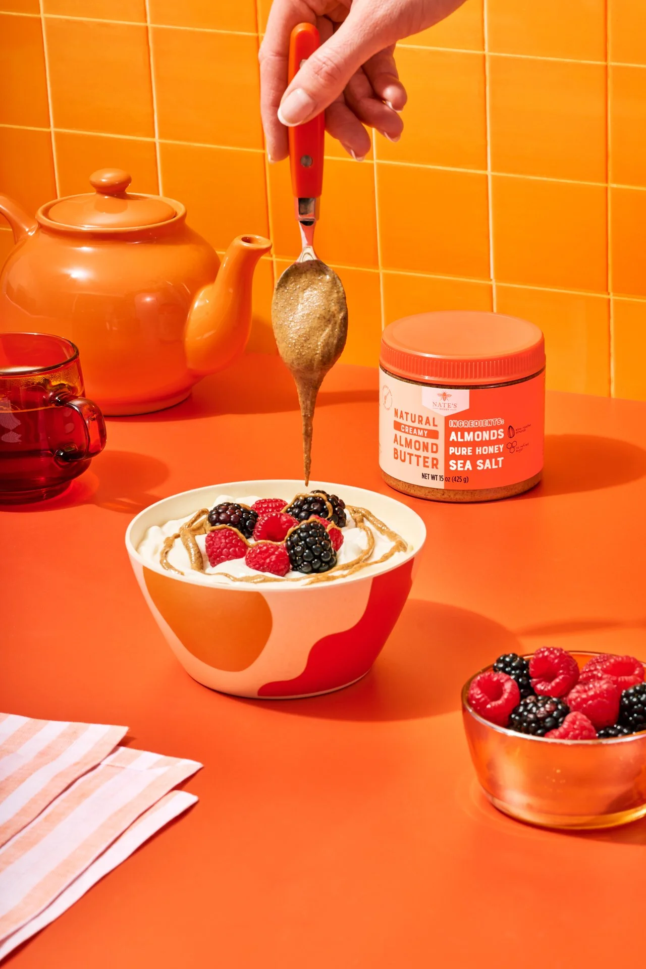 Commercial food product photography of nate's honey almond butter being poured from a spoon over a food styled yogurt bowl.